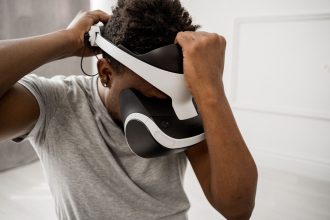 Homem ajusta um headset de realidade virtual em um ambiente interno bem iluminado.
