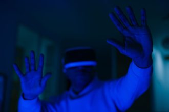 Homem usando headset de realidade virtual e interagindo com as mãos em um ambiente iluminado por luz azul.