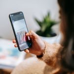 Pessoa mostra no celular uma imagem de peças de vestuário durante uma busca visual em ambiente doméstico.